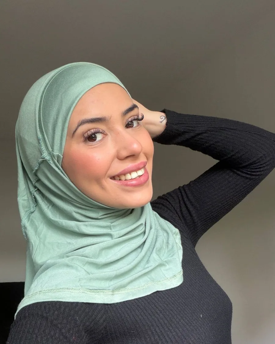 Amina in a sage green hijab and a black long-sleeved top, photographed indoors in soft daylight